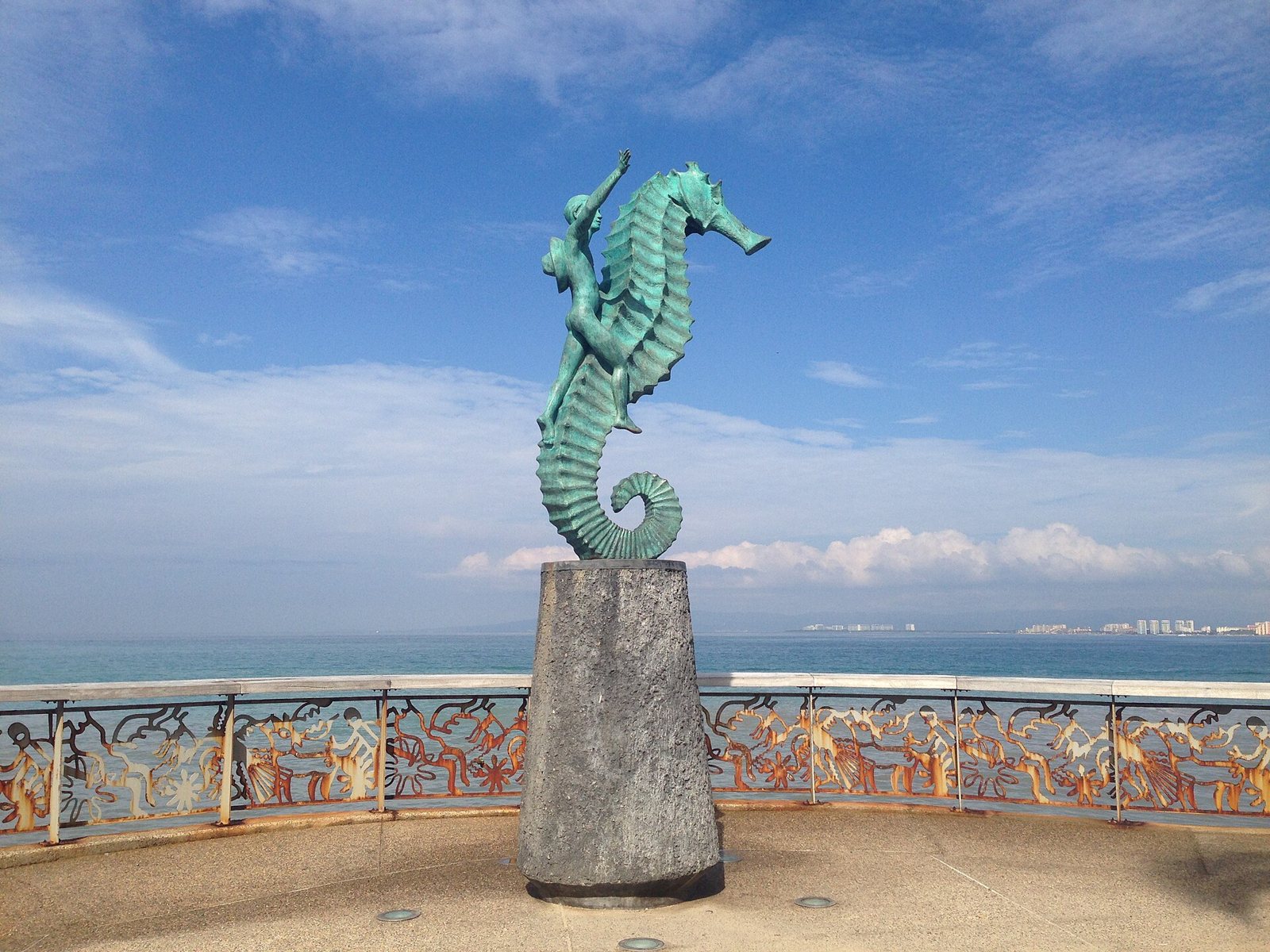 Escultura de bronce de un niño montado en un caballito de mar frente a la Bahía de Banderas