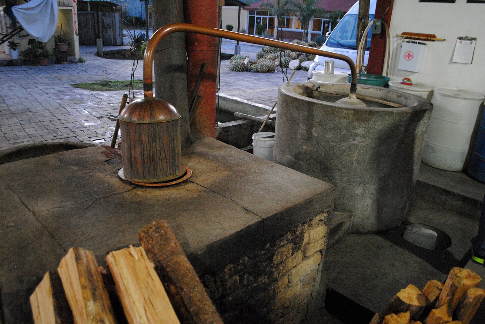 Alambique de cobre sobre un horno de piedra junto a un tanque de enfriamiento y leña
