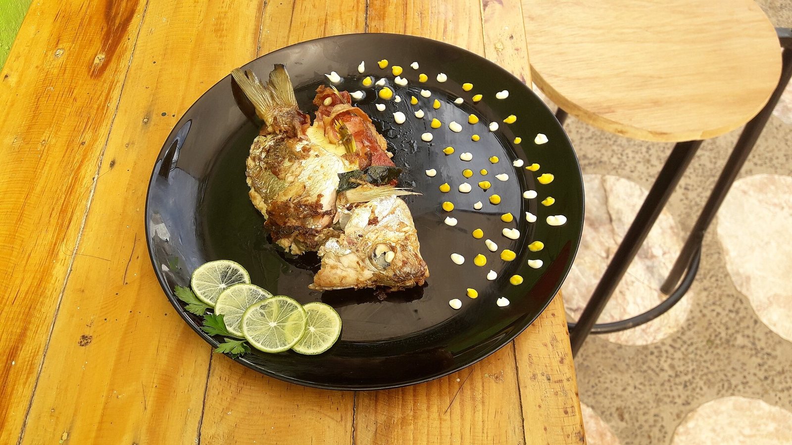 Pescado zarandeado abierto en un plato negro con limones, sobre una barra de madera