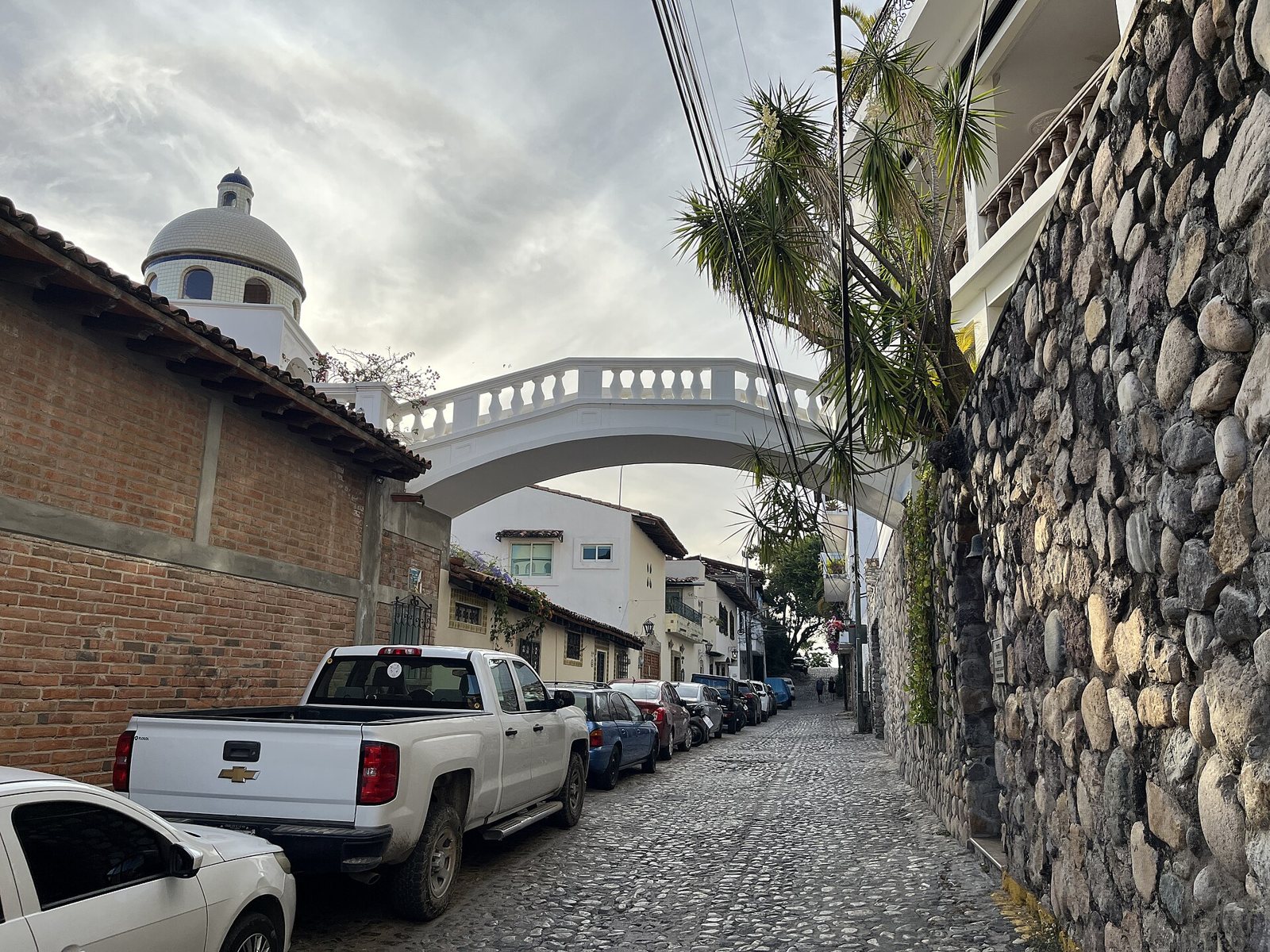 Calle empedrada en el centro de Puerto Vallarta con un puente blanco de balaustrada que cruza por encima entre dos casas