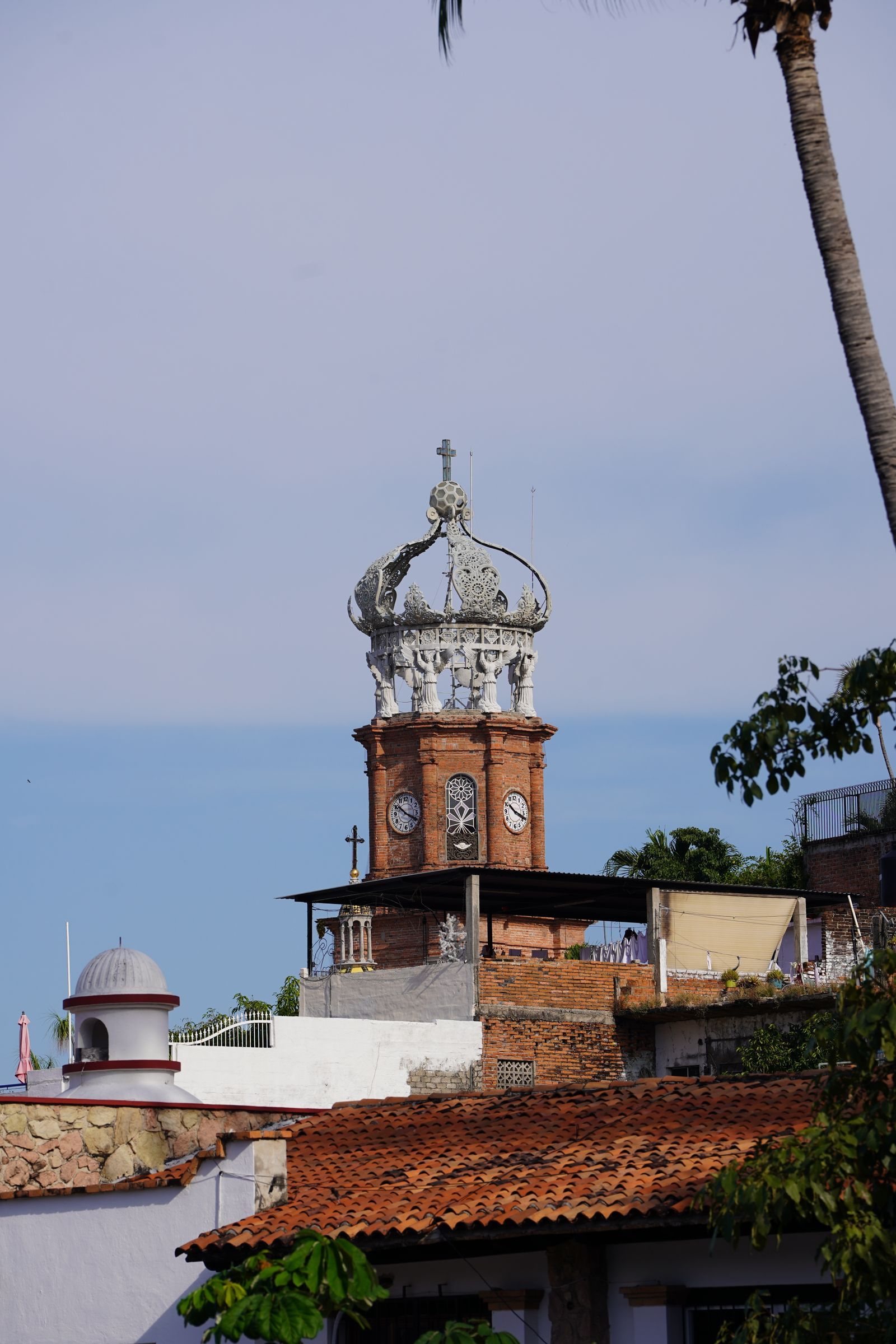 Torre de ladrillo con reloj y corona blanca de la parroquia de Puerto Vallarta, sobre techos de teja