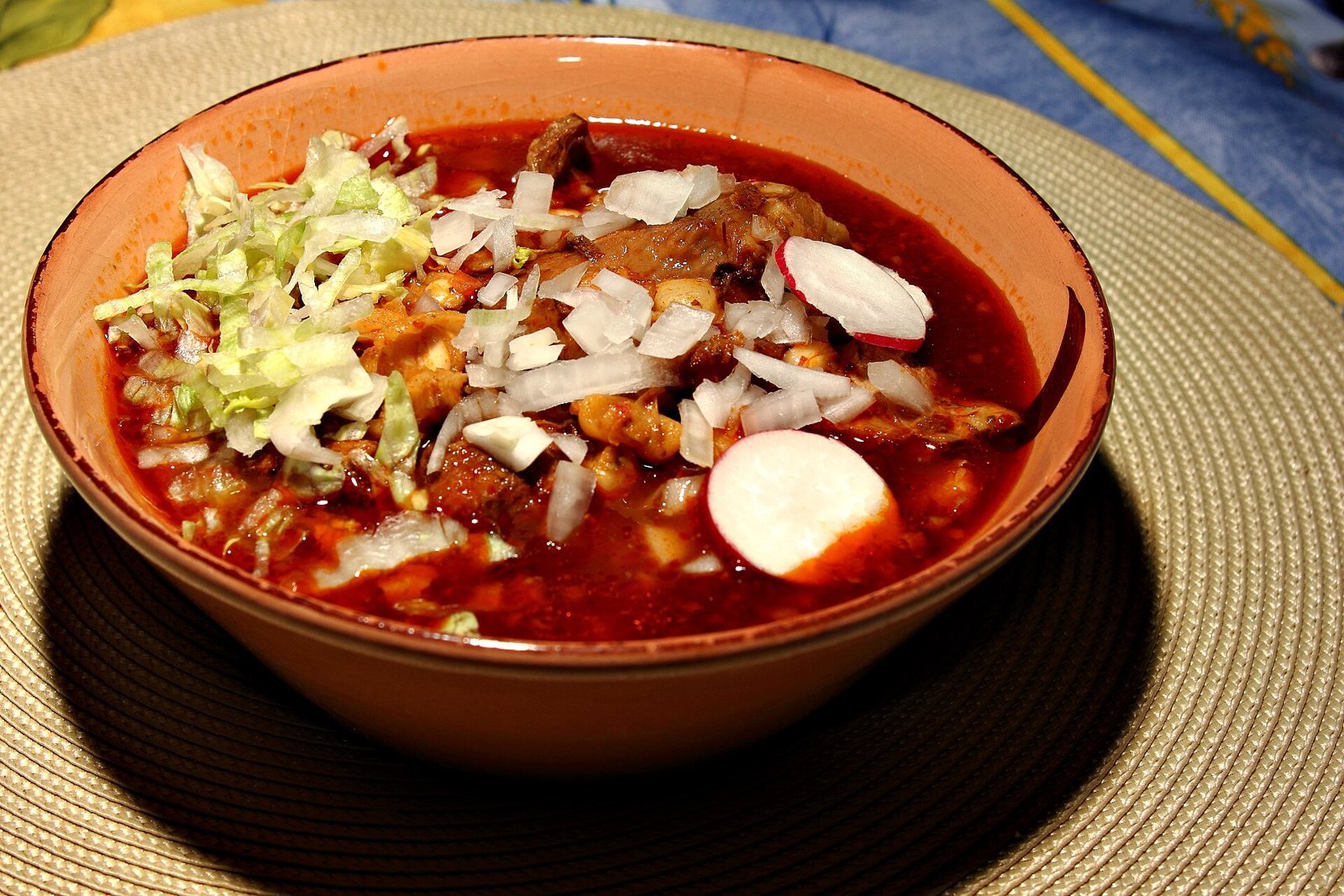 Plato hondo de pozole rojo con carne de cerdo, granos de maíz, lechuga, cebolla picada y rodajas de rábano