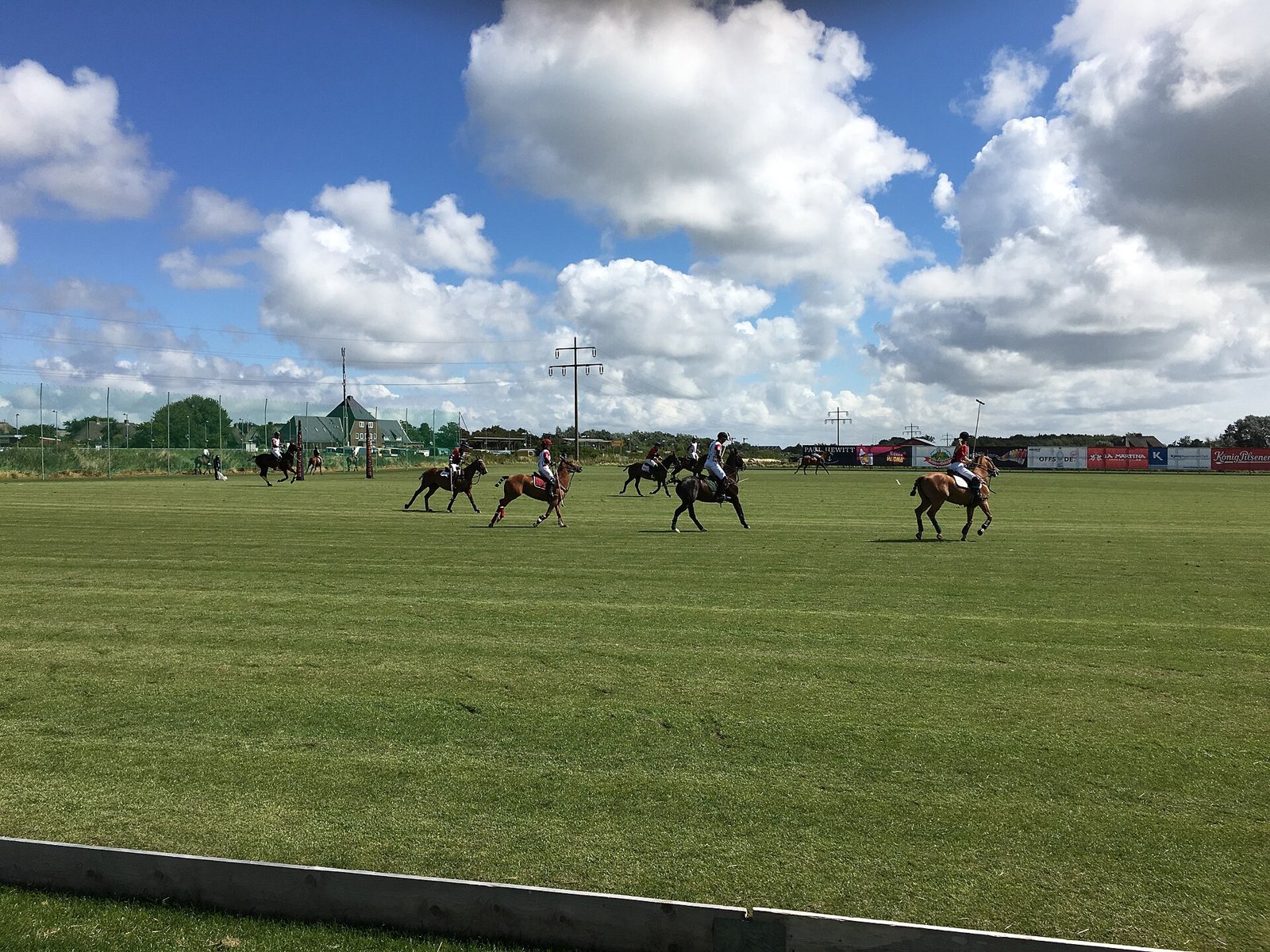Vista amplia de una cancha de polo con varios jinetes en juego bajo un cielo azul con nubes