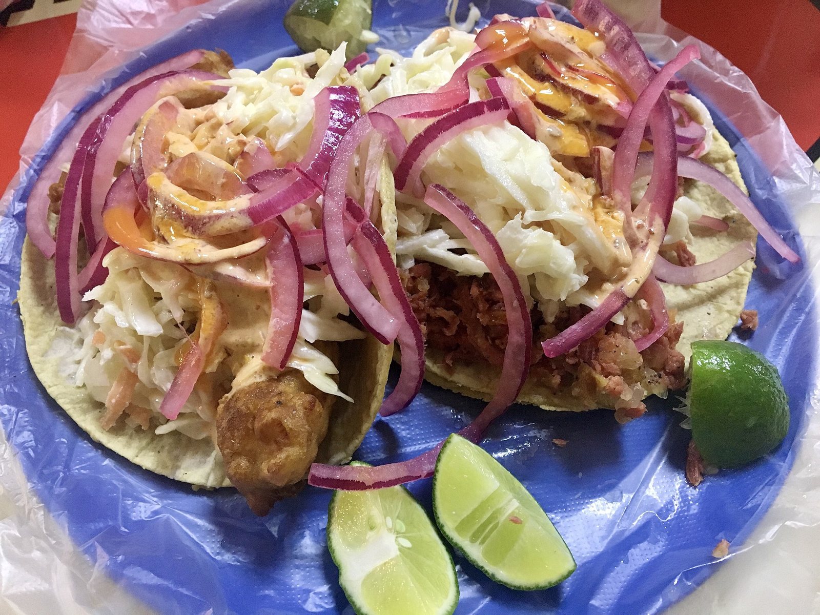 Dos tacos de pescado capeado con col, cebolla morada, aderezo cremoso y limones en un plato