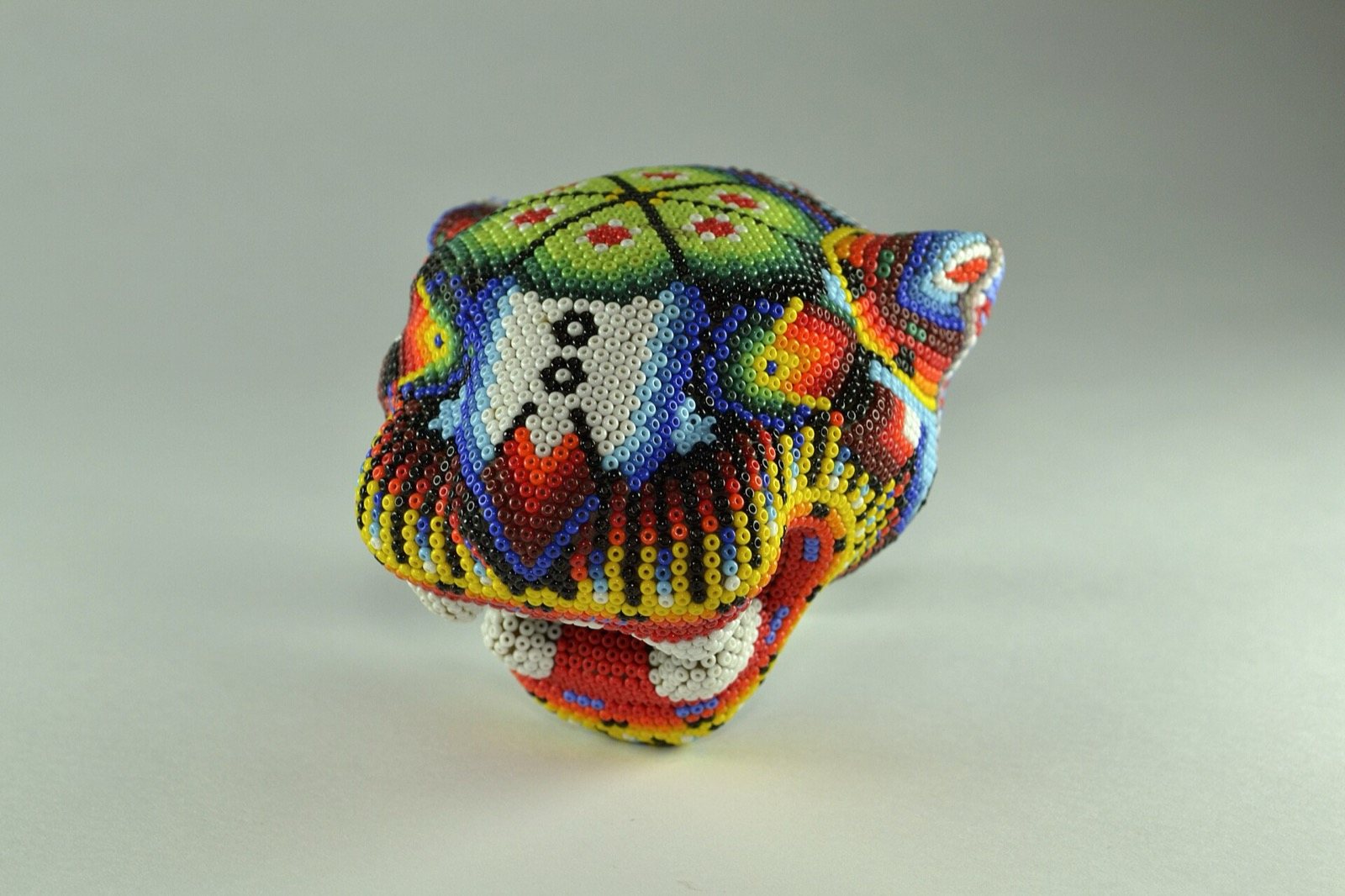Cabeza de jaguar cubierta por completo de chaquira de colores, sobre fondo gris claro