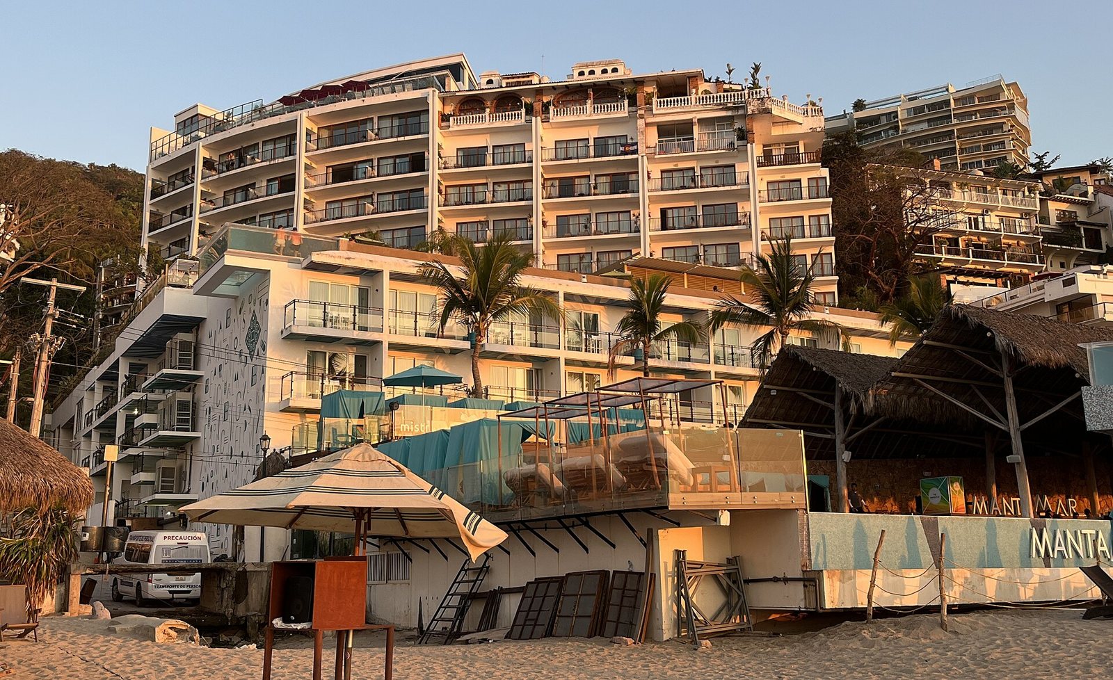Torres blancas del hotel Almar con balcones y, al pie, el club de playa con camastros turquesa sobre la arena de Playa Los Muertos, con luz dorada de la tarde