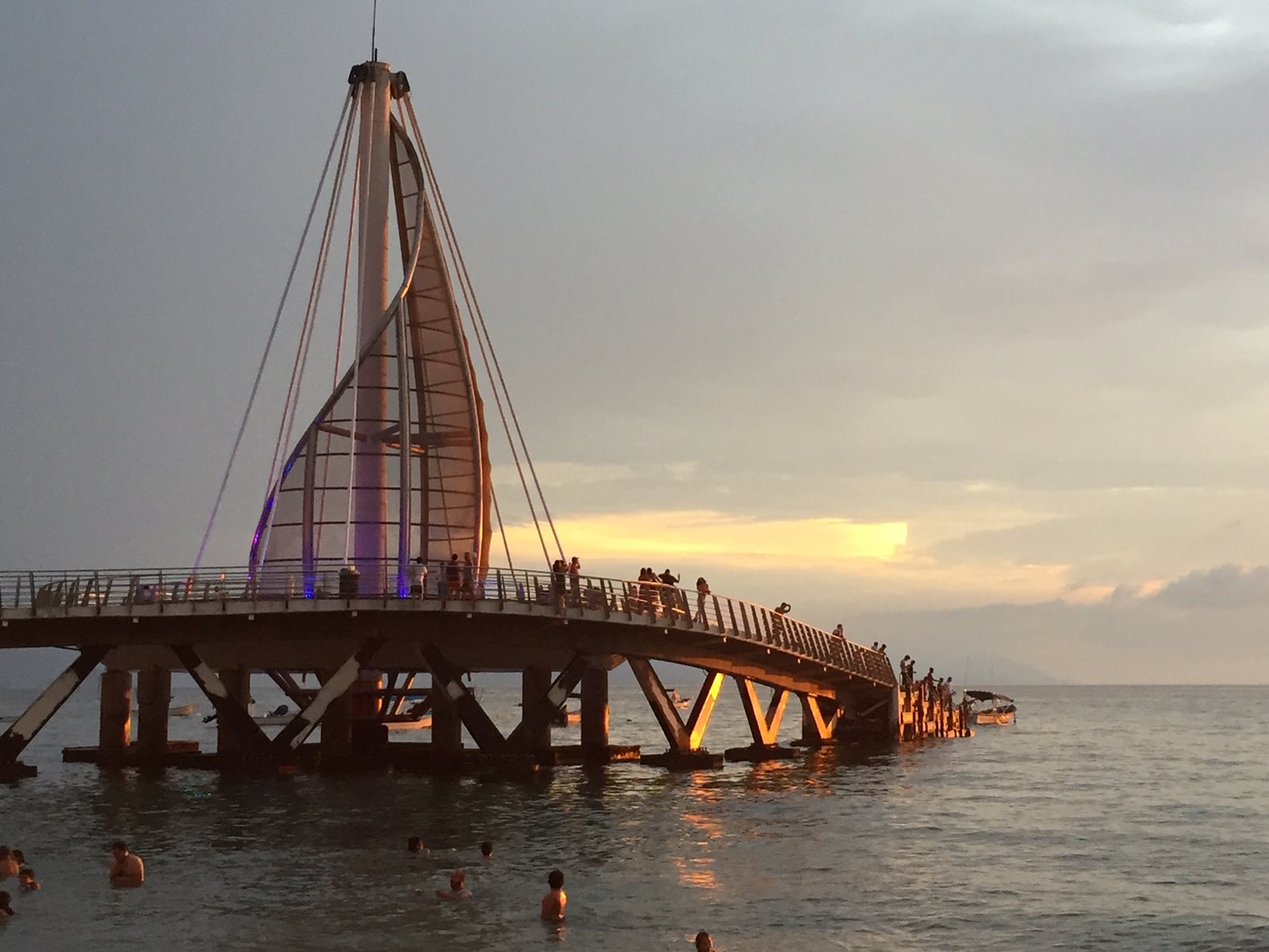 Muelle de Playa de los Muertos con su estructura en forma de vela iluminada al atardecer y gente caminando sobre él