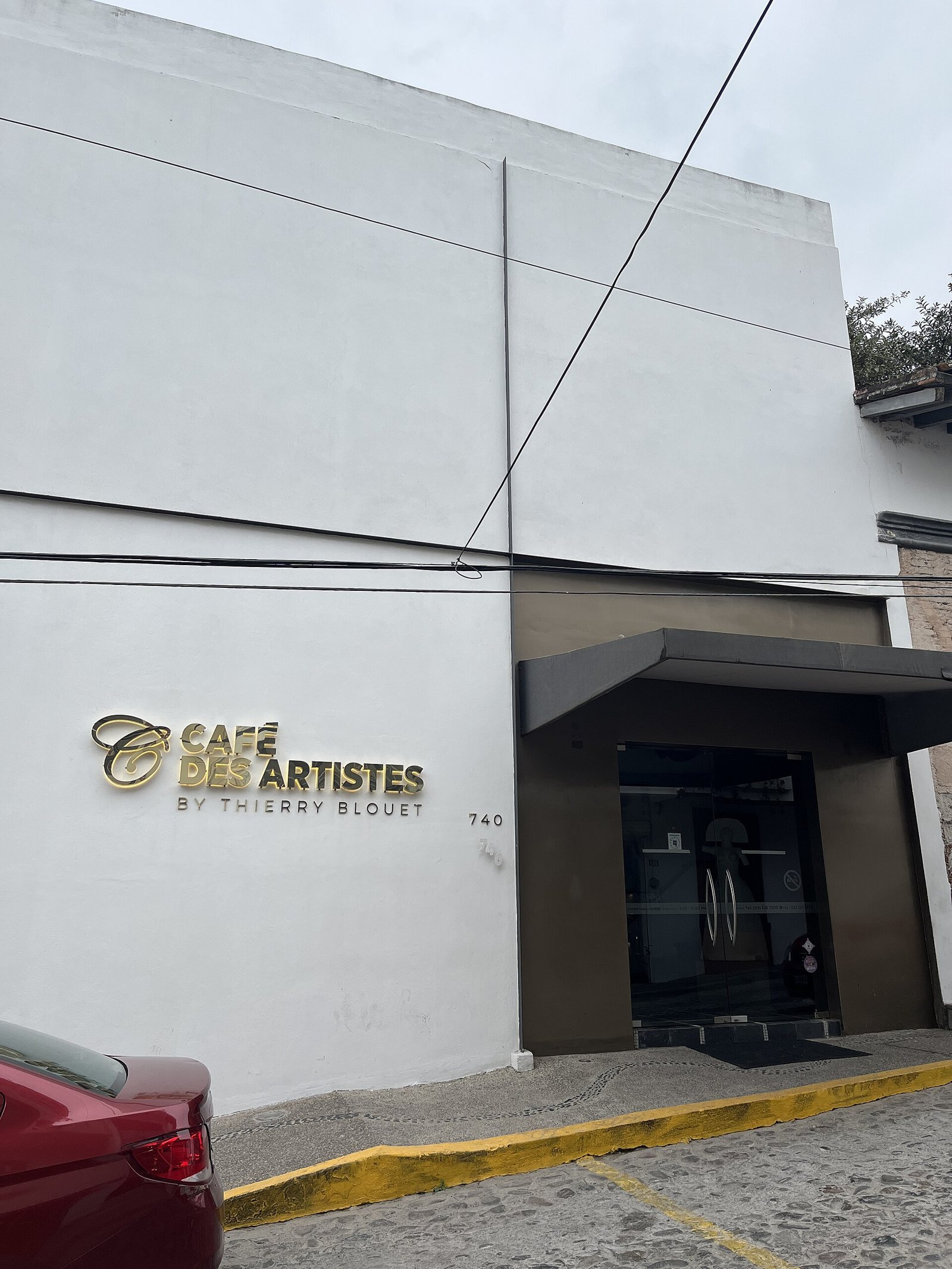 Fachada blanca de Café des Artistes by Thierry Blouet con letras doradas y el número 740, sobre una calle empedrada del centro