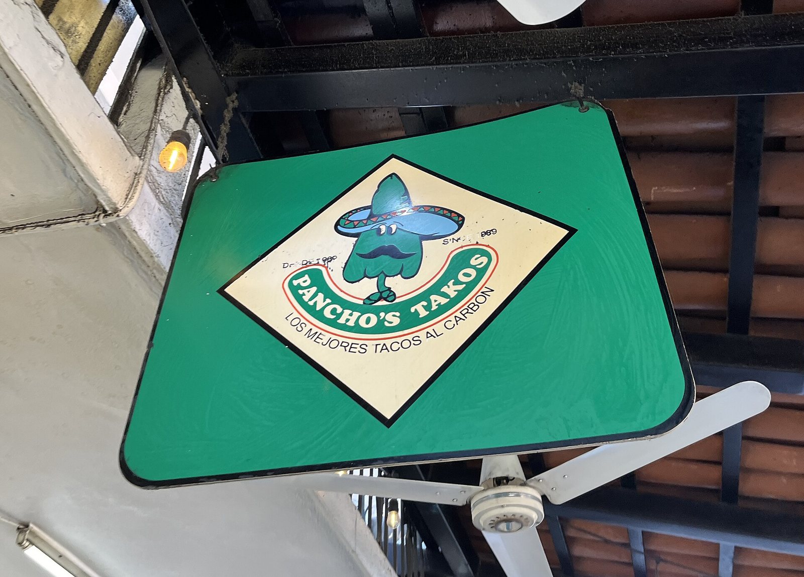 Letrero verde colgante de Pancho's Takos con un personaje con sombrero y la frase Los mejores tacos al carbón