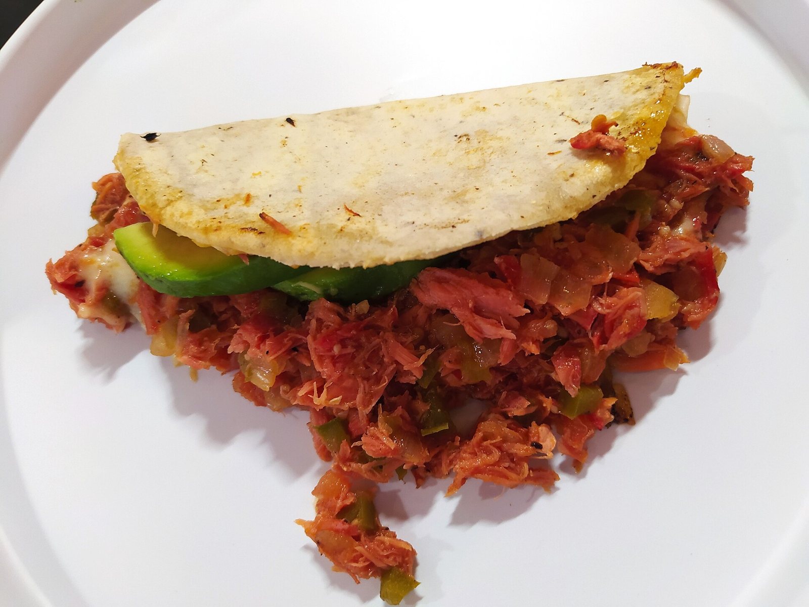 Quesadilla de tortilla de maíz rellena de marlín guisado con jitomate y una rebanada de aguacate, en plato blanco
