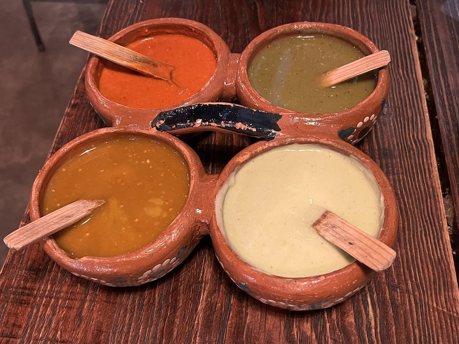 Salsero de barro con cuatro salsas de colores rojo, verde, naranja y crema, con palitas de madera
