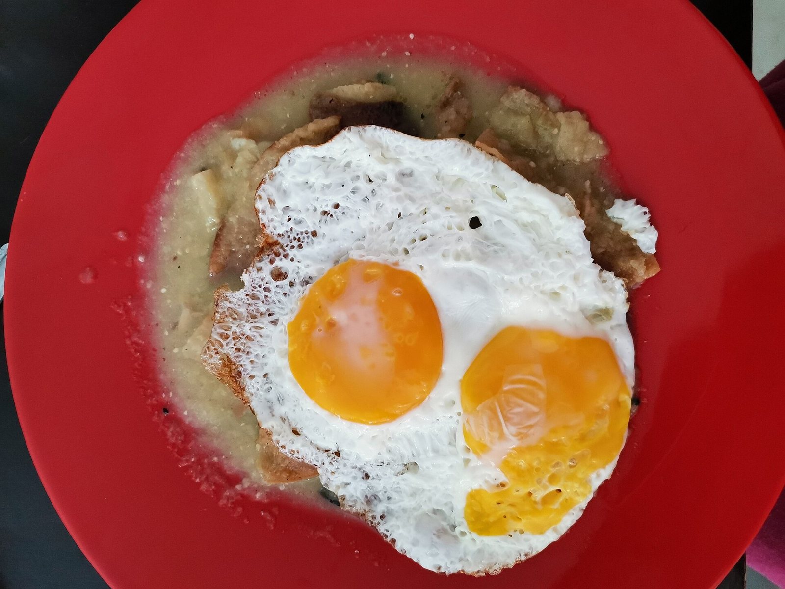 Plato rojo con chilaquiles en salsa verde y dos huevos estrellados encima