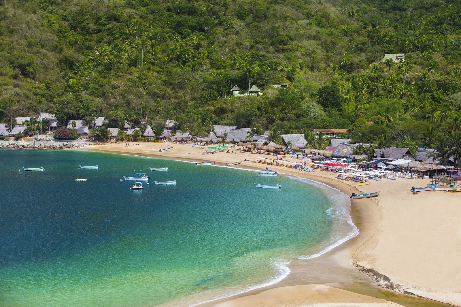 Vista desde lo alto de la playa de Yelapa, con agua turquesa, pangas fondeadas, palapas y cerros cubiertos de palmeras